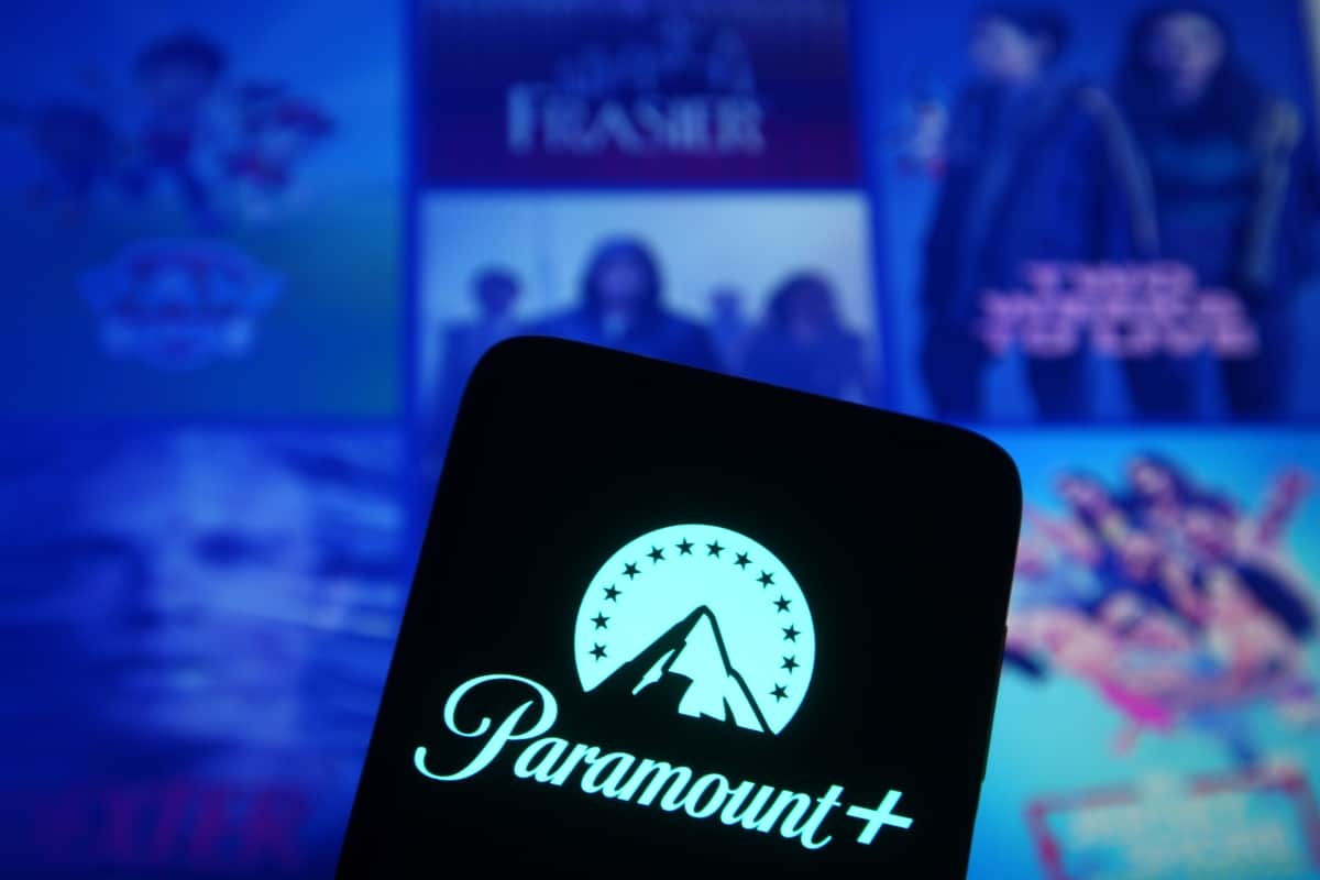 Celular com logomarca do Paramount+ na tela e, ao fundo, pôsteres de títulos do catálogo do streaming
