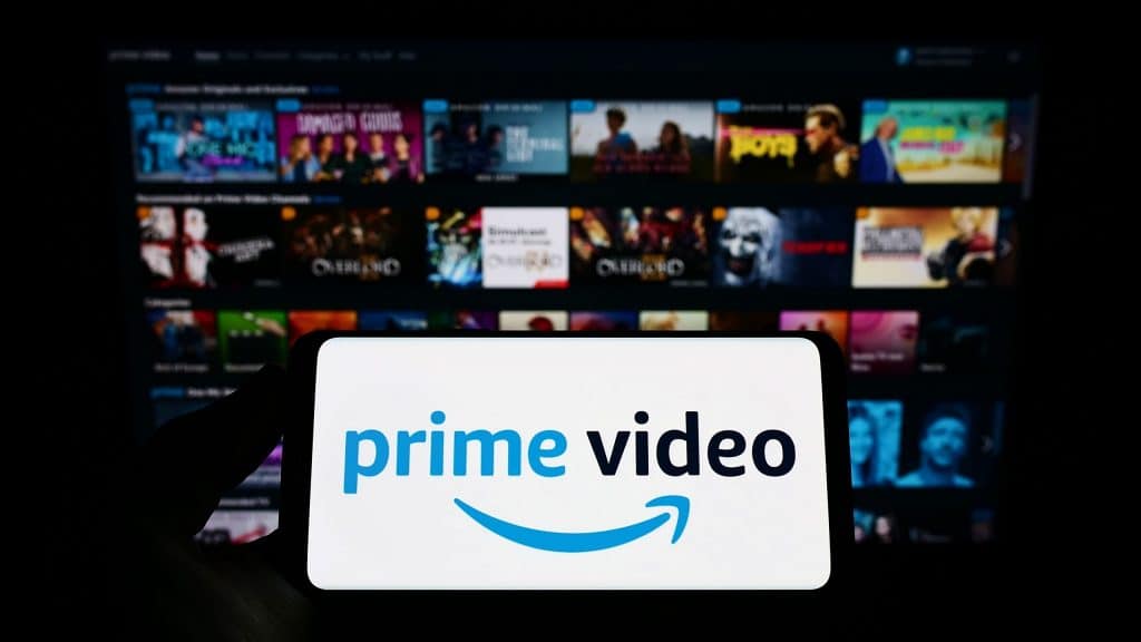 Logo do Prime Video em smartphone com fundo de catálogo do Prime Video na TV