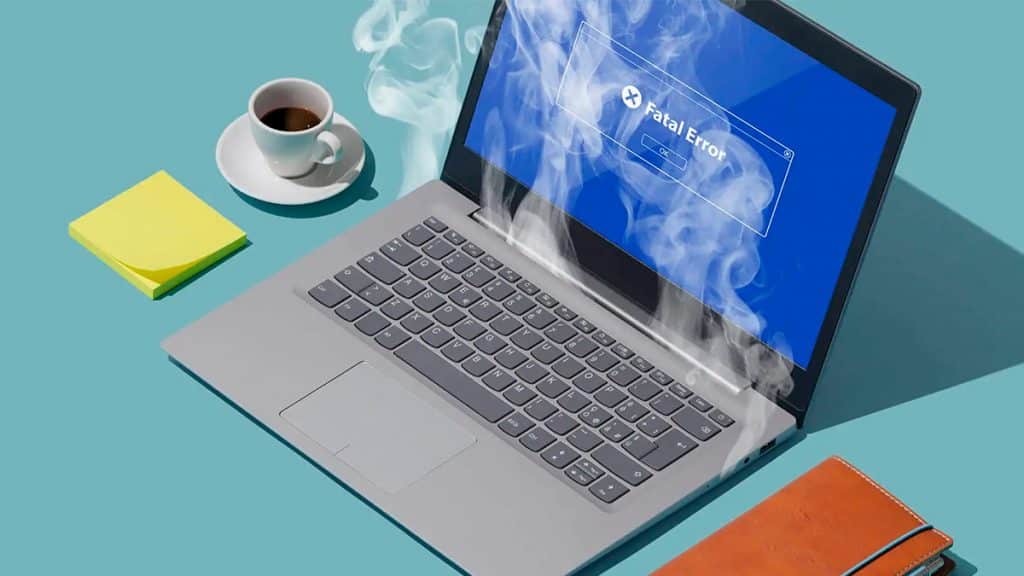 Notebook superaquecendo ao lado de café e caderno de anotações