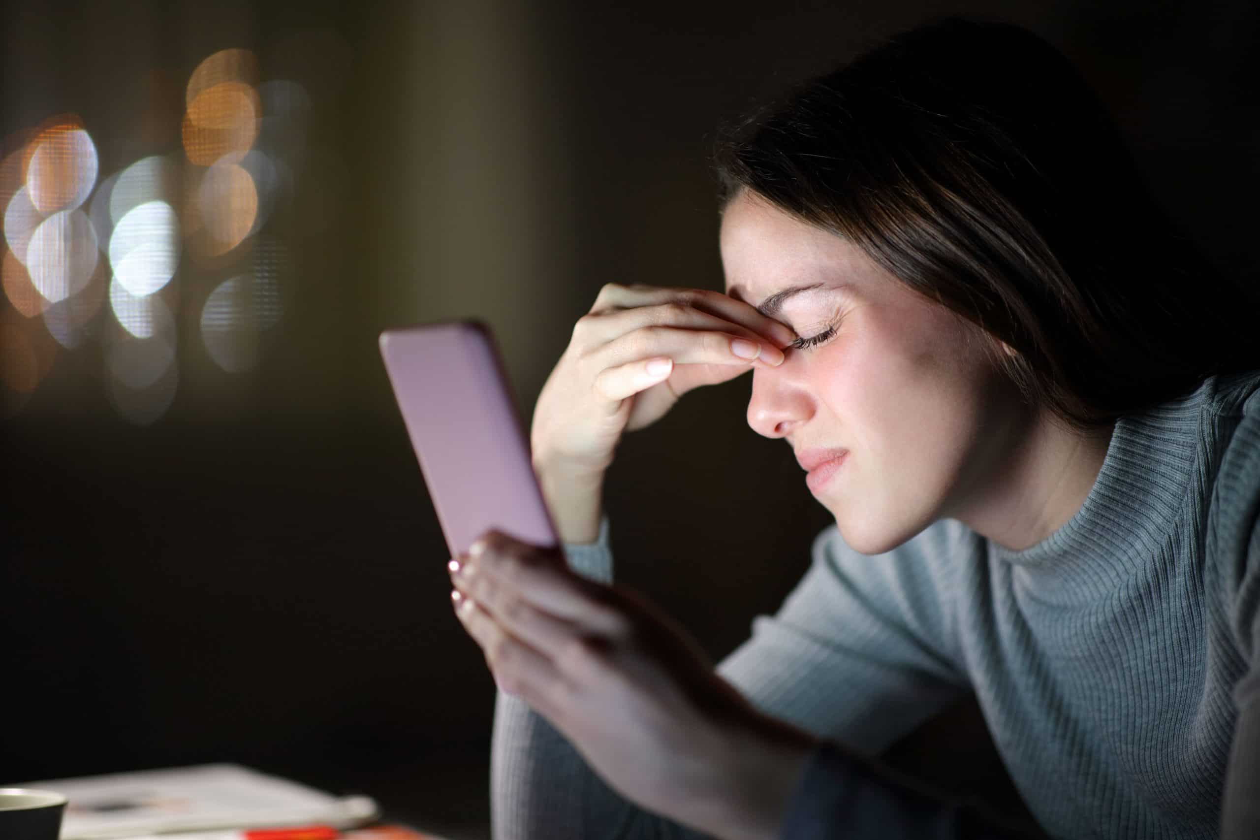 Imagem de mulher pressionando a cabeça e olhando para o celular para contextualizar se o a radiação faz mal