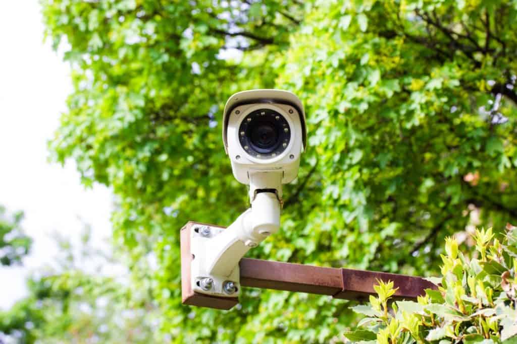 Câmera de vigilância CCTV IP instalada em um ambiente verde, escondida por folhagens. Conceito de segurança e controle de propriedade.