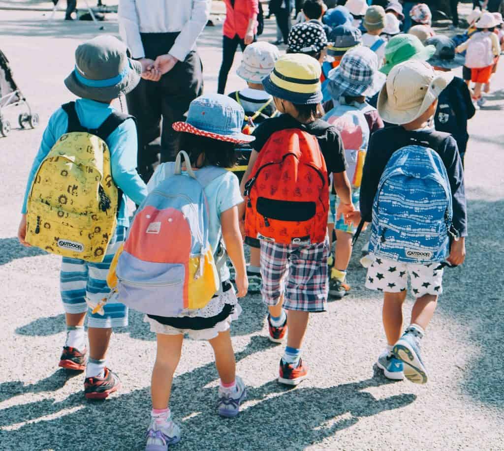 10 portais para poupar na aquisição de material escolar Guia Região dos Lagos 9 Imagem retratando várias crianças a caminho da escola, carregando mochilas nas costas