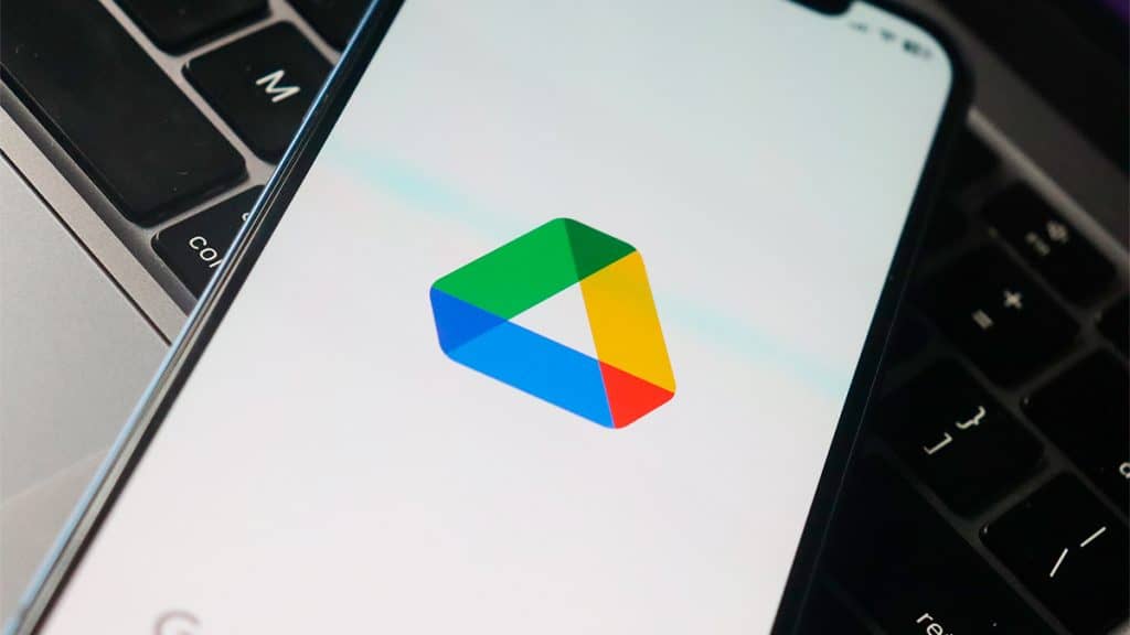 Logotipo do Google Drive no aplicativo aberto num iPhone sobre um Macbook