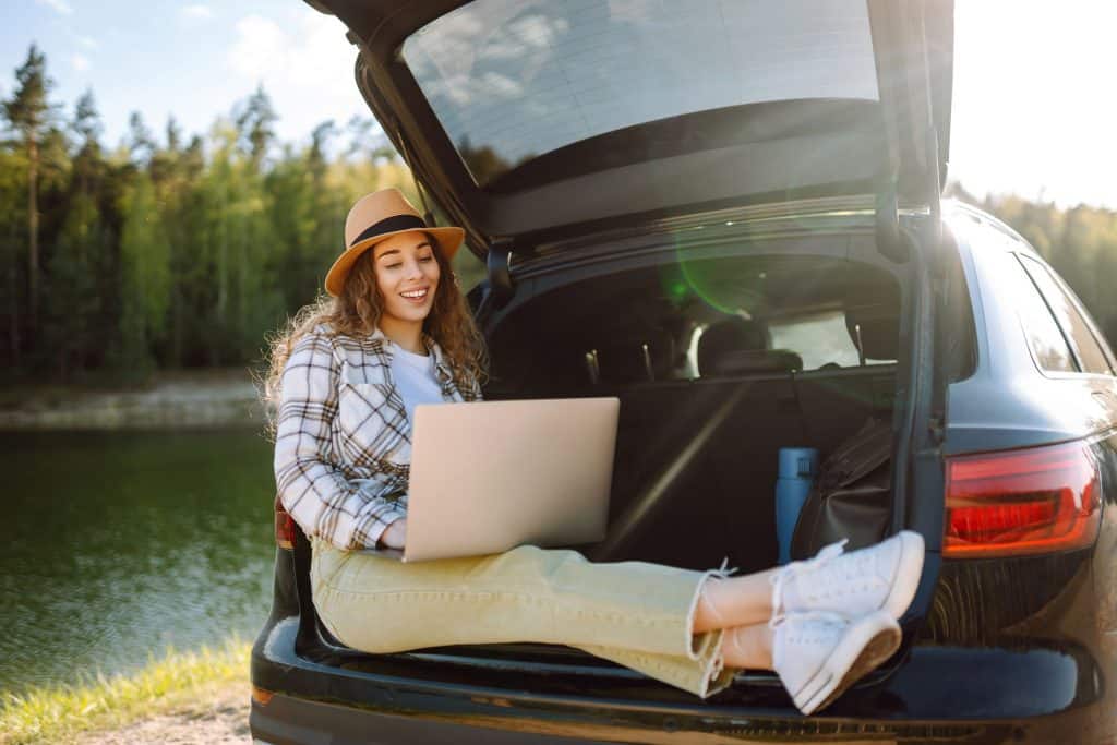 4 sugestões para cuidar do laptop e evitar quedas ou riscos Guia Região dos Lagos 7 Mulher utilizando o laptop no banco de trás de um carro, mostrando a importância do cuidado ao manusear.