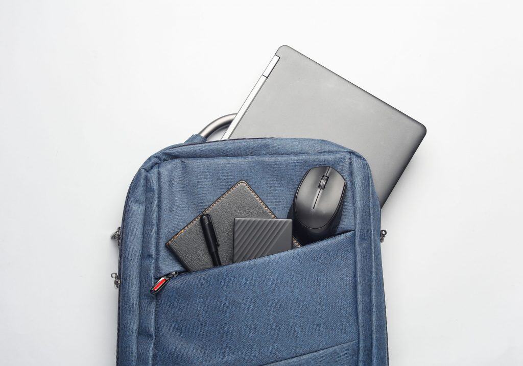 4 sugestões para cuidar do laptop e evitar quedas ou riscos Guia Região dos Lagos 5 Mochila com notebook e outros gadgets dispostos sobre fundo branco, ideal para transporte seguro.