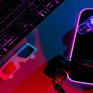 Vista superior de configuração de teclado gamer neon, controladora pro gaming, mesa iluminada junto com fone de ouvido, teclado e luzes neon do computador.