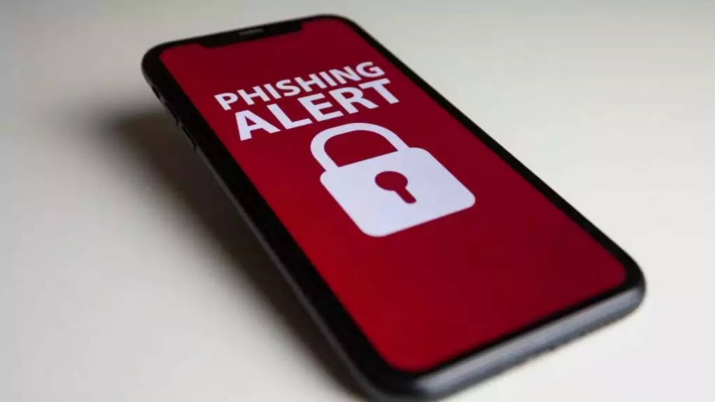Descubra se seu iPhone foi invadido! 5 sinais para ficar atento Guia Região dos Lagos 4 Munique, Alemanha; 12 de novembro de 2022: Um iPhone XR com Alerta de Phishing escrito na tela. Iphone com tela em vermelho e desenho de cadeado e alerta em branco.